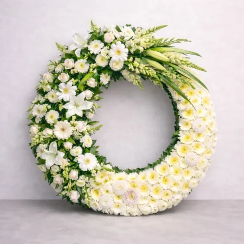Corona para difunto diseño moderno media luna con follaje verde y flores blancas.