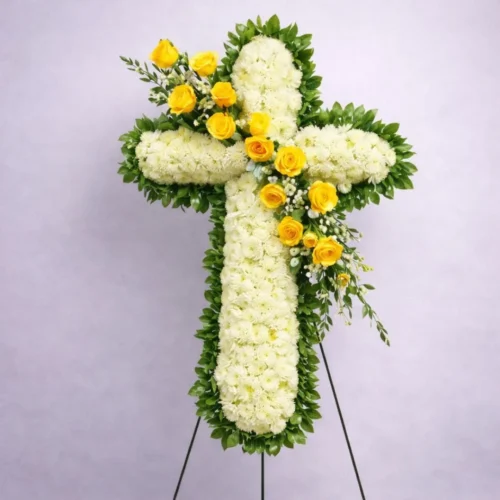 Cruz de flores blancas para funeral con banda transversal de rosas amarillas.