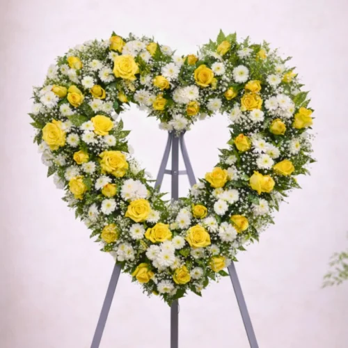 corona funeraria en forma de corazón con rosas amarillas y flores blancas sobre pedestal funerario