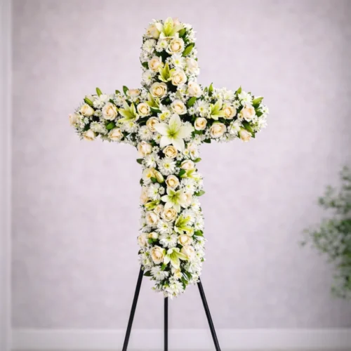 arreglo funerario en forma de cruz con rosas blancas y lirios sobre pedestal