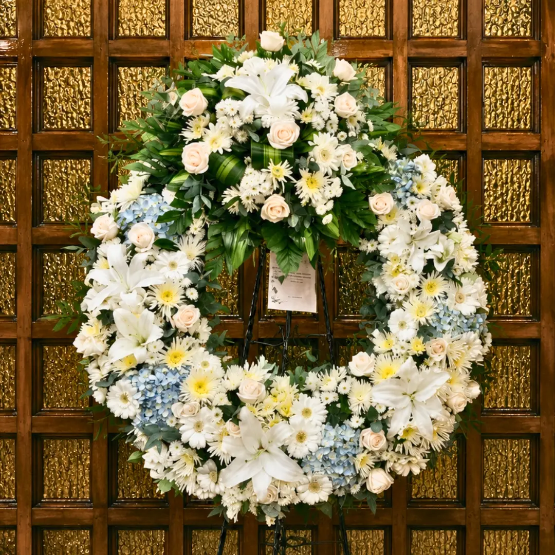 Corona fúnebre blanca con lirios, rosas y hortensias celestes en Guatemala